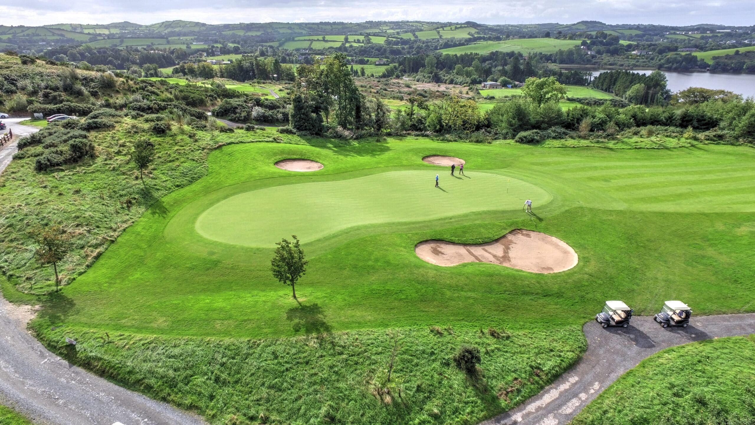 Aerial perspective of a golf course with expansive green lawns and tranquil water bodies, surrounded by trees.